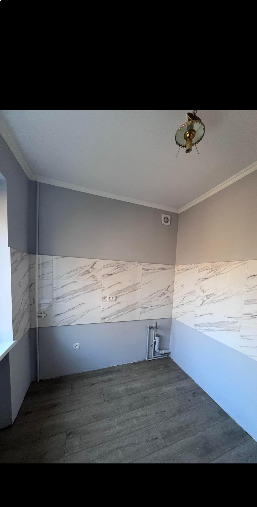 Wykończona łazienka z szarymi ścianami, marmurkowymi płytkami do połowy wysokości i panelami podłogowymi imitującymi drewno, widoczny grzejnik i lampa sufitowa w stylu retro.