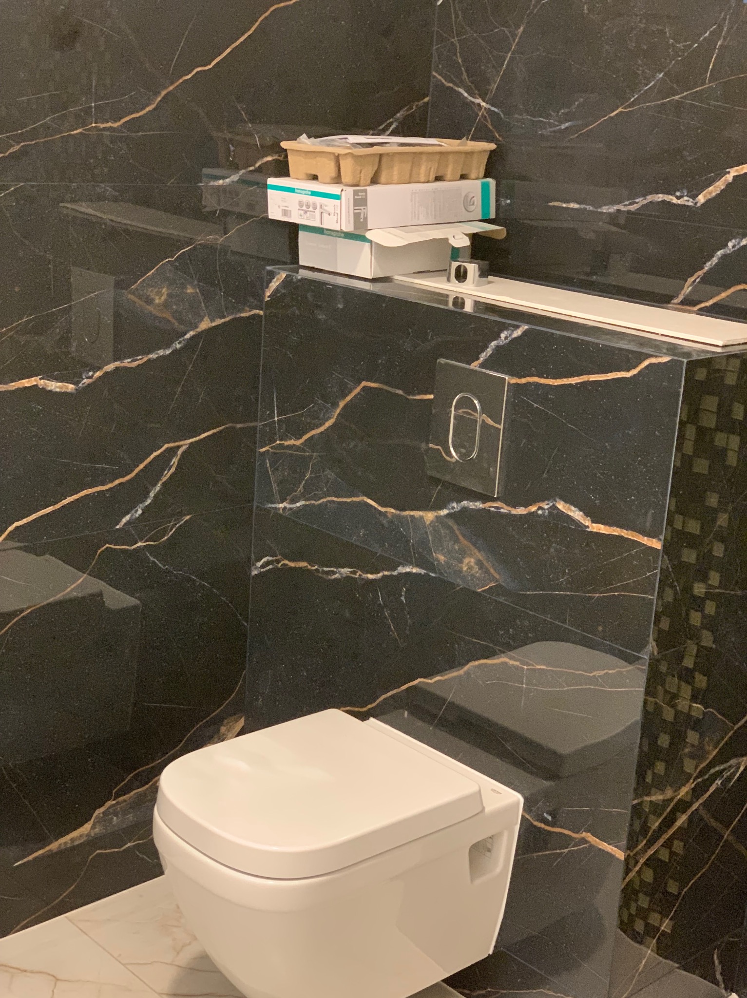 Podwieszana toaleta w trakcie montażu w Ząbkach, z widocznymi pudełkami po elementach instalacyjnych na tle czarnej ściany z marmurowym wzorem.