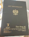 Czarne etui na akt notarialny z godłem Polski i napisem 'Akt Notarialny' w złotym kolorze, poniżej nazwa kancelarii notarialnej Zine Abass Ali.