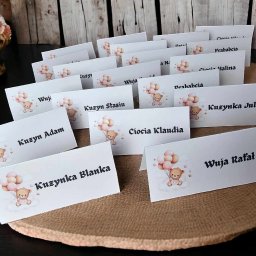 DIA MODA Patrycja Jelak - Personalizowane winietki na stół z imionami gości, ozdobione motywem misia z balonami, ustawione na okrągłej podkładce z naturalnego materiału, idealne na przyjęcie.