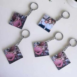 DIA MODA Patrycja Jelak - Kwadratowe breloczki z metalowym łańcuszkiem i kółkiem, z nadrukowanymi zdjęciami dzieci na białym tle, obok doniczki z zieloną rośliną.