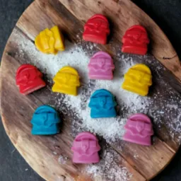 Ręcznie robione, kolorowe czekoladki w kształcie torebek, ułożone na drewnianej desce posypanej cukrem pudrem, widok z góry.