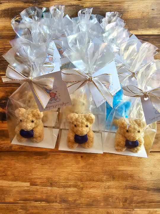 Ręcznie robione mydlane misie w przezroczystych torebkach z kokardkami, idealne jako upominki na baby shower, na drewnianym tle.
