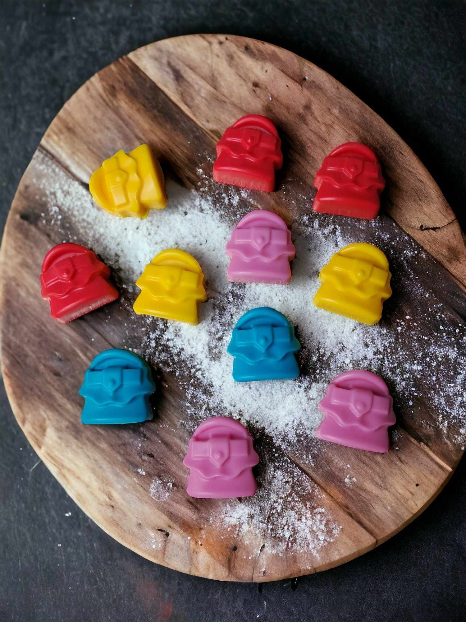 Ręcznie robione, kolorowe czekoladki w kształcie torebek, ułożone na drewnianej desce posypanej cukrem pudrem, widok z góry.