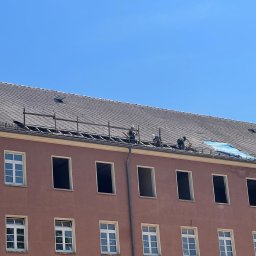 Sebastian Buda firma wykonczeniowa - Trzech robotników na dachu budynku podczas naprawy poszycia dachowego z wykorzystaniem rusztowania i plandeki zabezpieczającej.