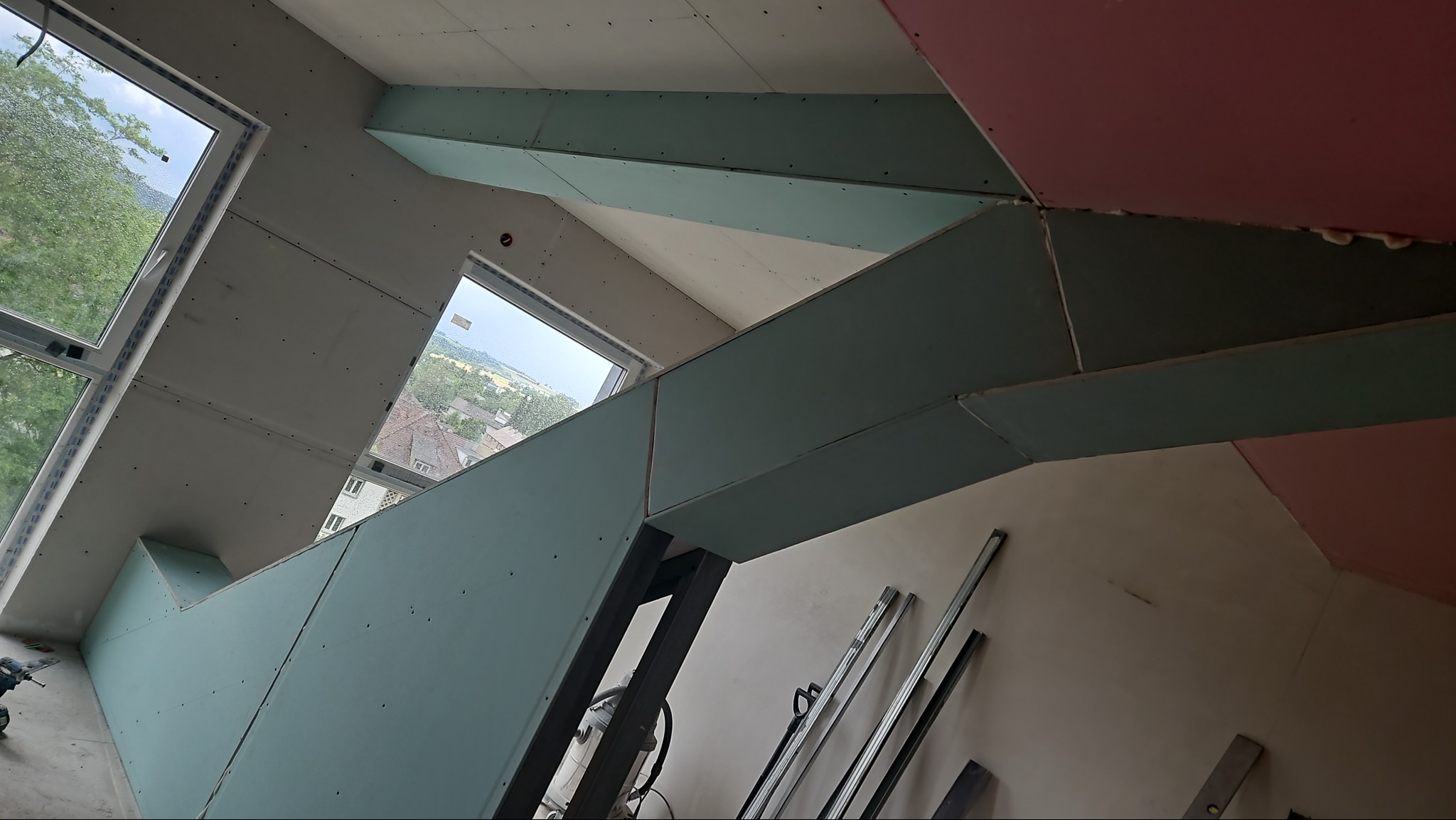 Skośne poddasze z oknami, w trakcie montażu płyt gipsowo-kartonowych na konstrukcji, widoczne profile i pianka montażowa.