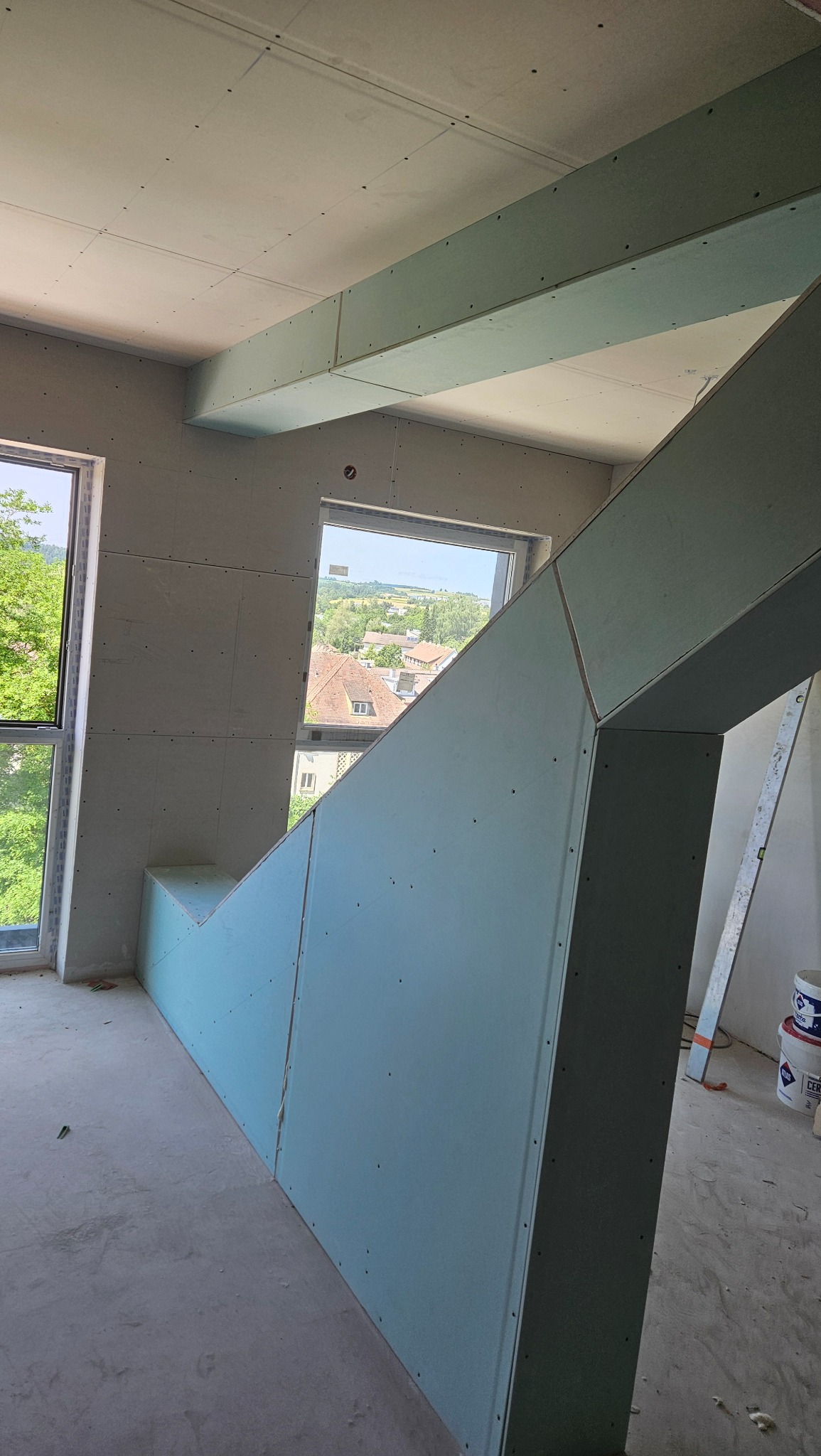 Montaż konstrukcji z płyt gipsowo-kartonowych w nowym budynku z widokiem na miasto przez okna.