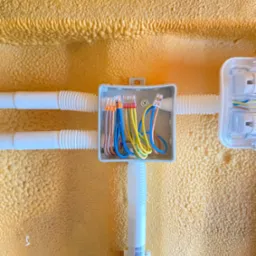 Połączenia przewodów w puszce instalacyjnej z widocznymi złączkami WAGO, umieszczonej na ścianie pokrytej pianką izolacyjną. Rury karbowane doprowadzają przewody.