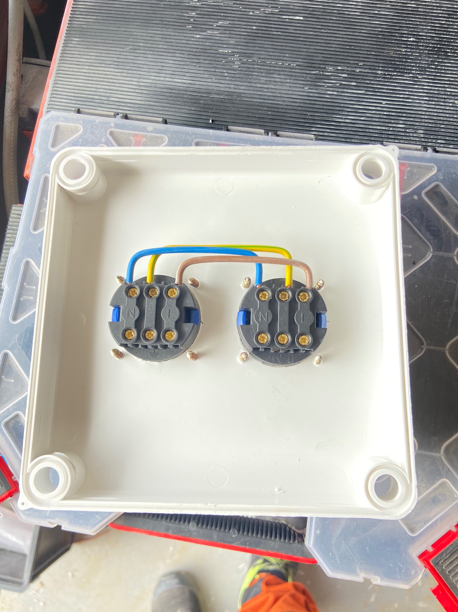 Dwa podwójne gniazda elektryczne z podłączonymi przewodami (niebieski, żółty, brązowy) zamontowane w białej puszce instalacyjnej, widok z góry, realizacja w Rynarzewie.