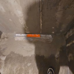 MasterOK OLEH VASYLOVSKYI - Przygotowanie podłoża pod prysznic w Poznaniu. Widoczny odpływ liniowy i surowy beton na ścianach. Etap prac wykończeniowych w łazience.