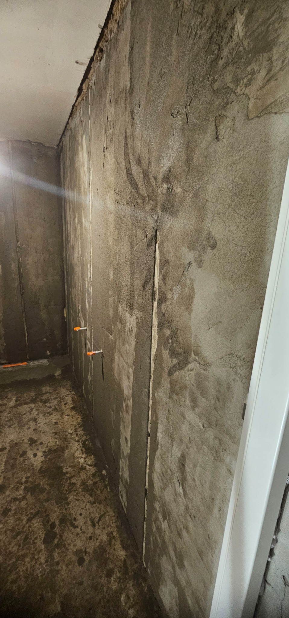 Surowa ściana w trakcie szpachlowania z widocznymi śladami po łatach i niedoskonałościami, przygotowywana do dalszych prac wykończeniowych w pomieszczeniu.