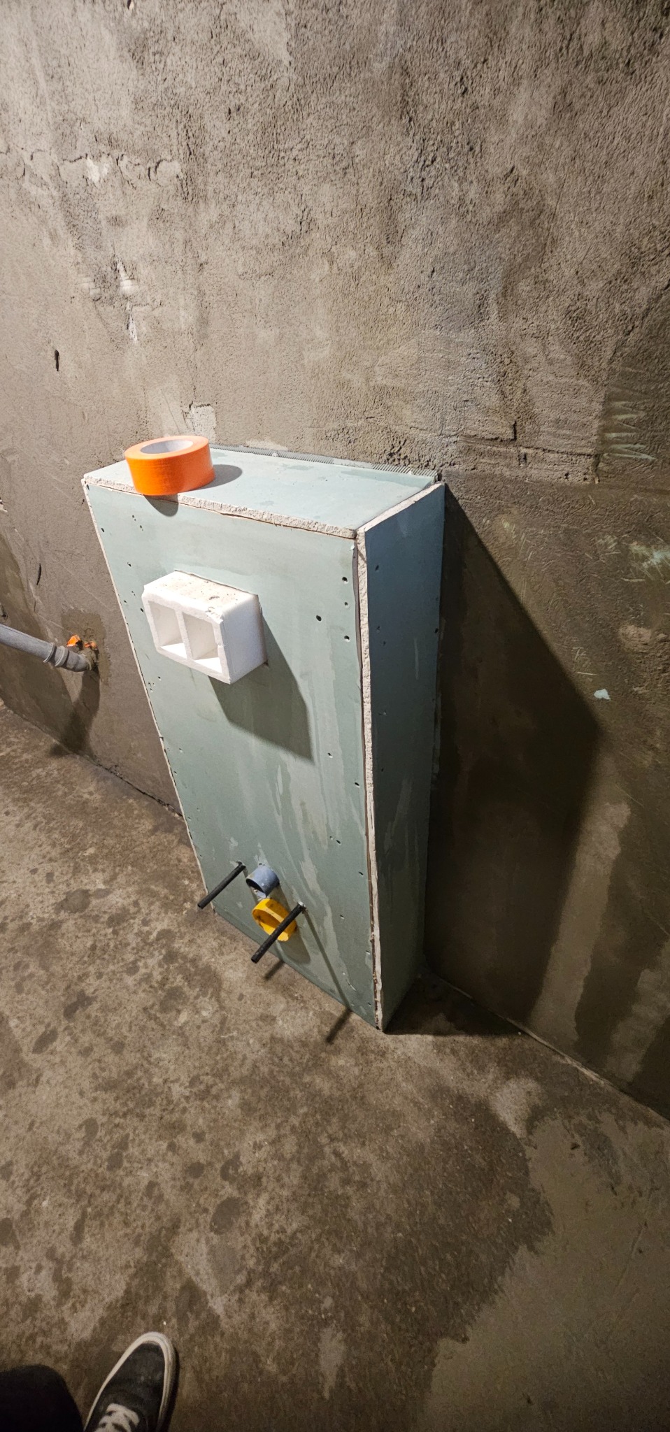 Konstrukcja z płyty gipsowej zabudowująca instalację wodną w surowej łazience, widoczne elementy mocujące i taśma malarska. Przygotowanie do wykończenia.