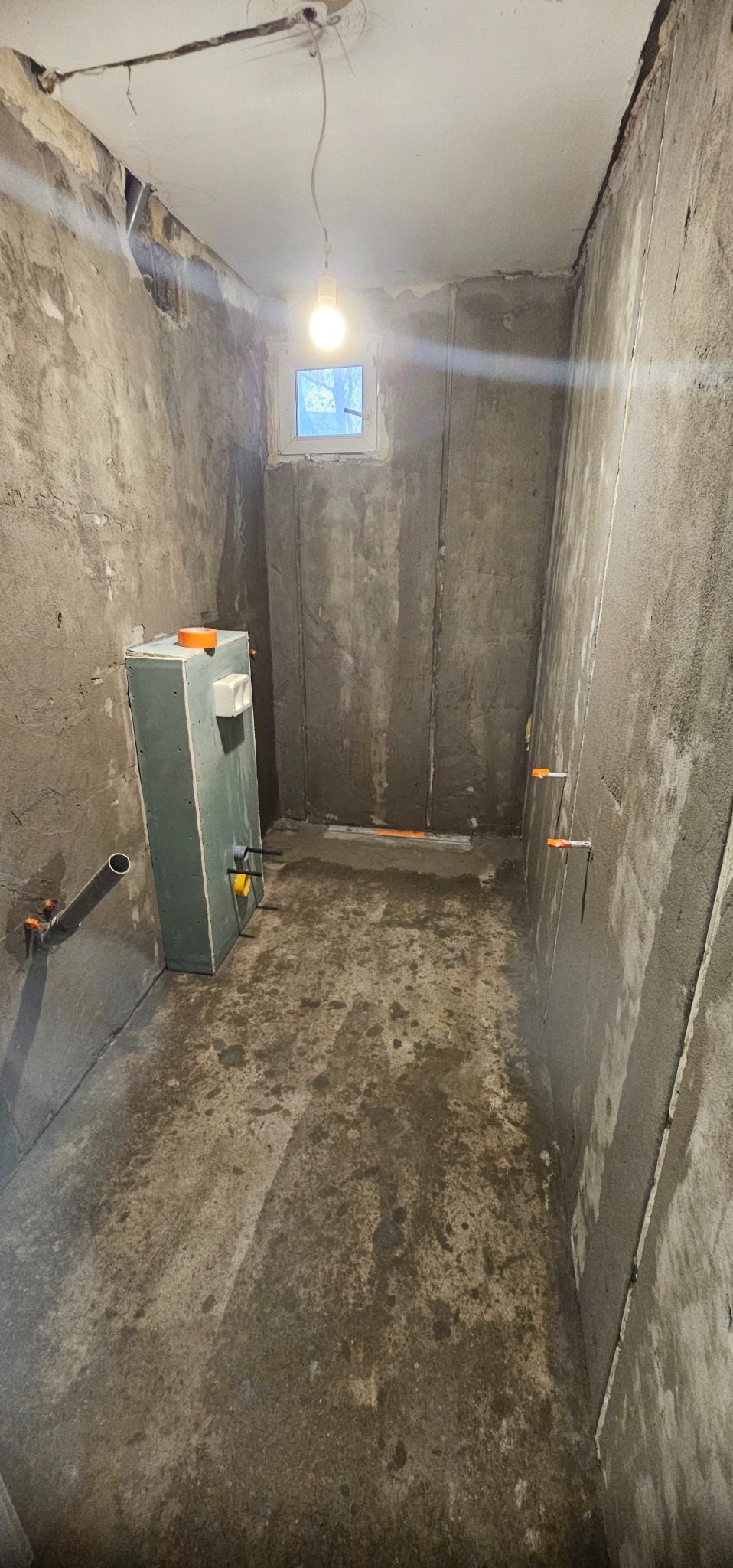 Surowa łazienka w trakcie wykańczania: szpachlowane ściany, instalacja podtynkowa, małe okno. Widoczne elementy instalacji wodno-kanalizacyjnej.