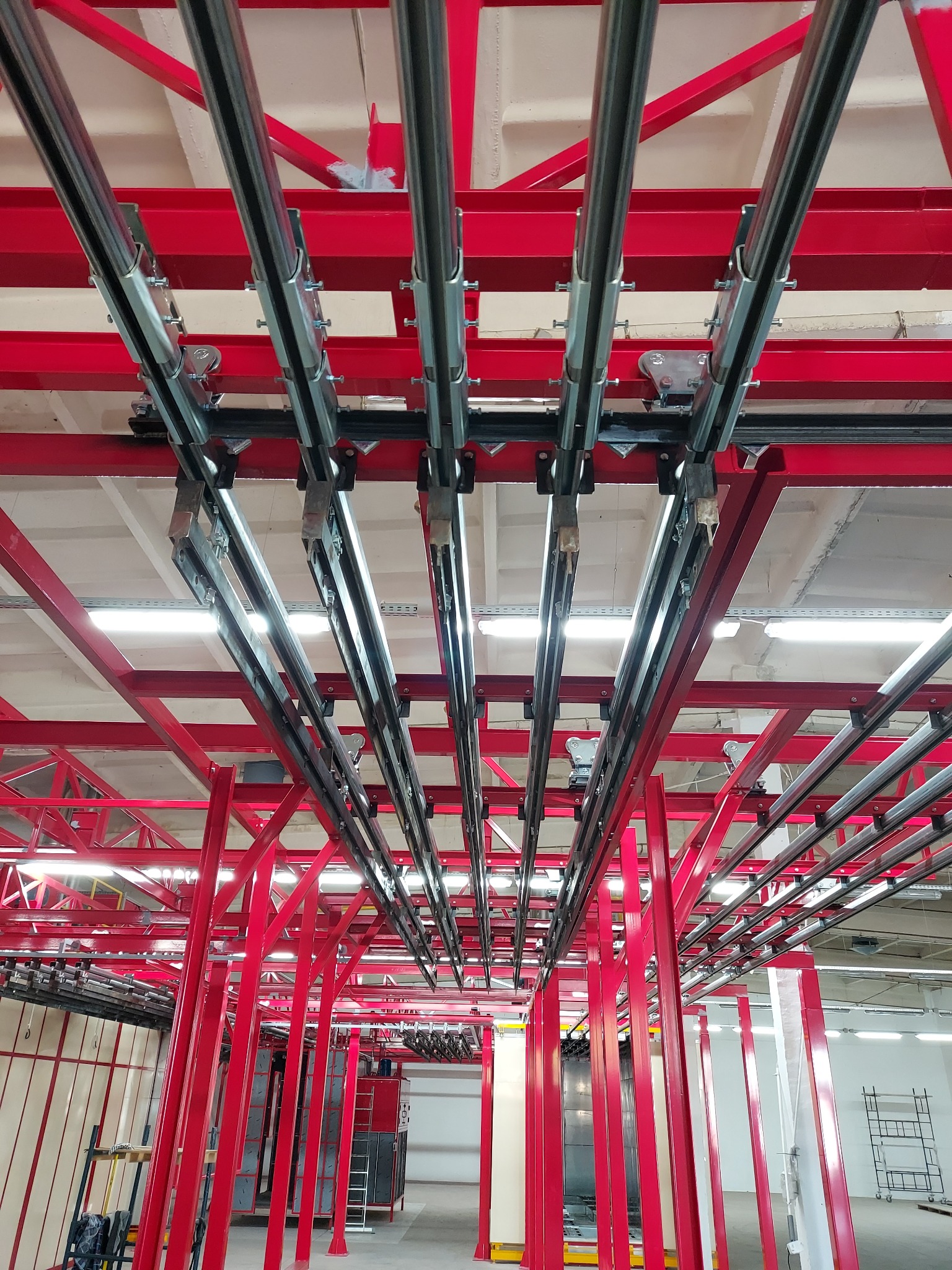 Czerwona stalowa konstrukcja sufitowa z zamontowanymi szynami transportowymi w hali przemysłowej.