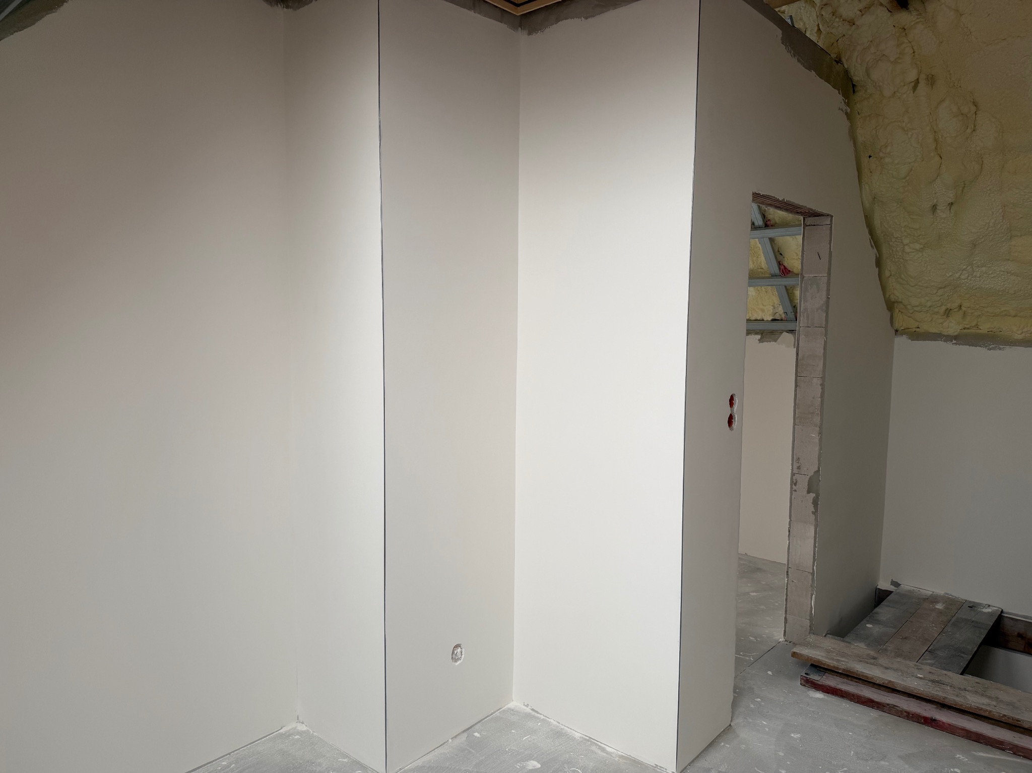 Wnętrze w trakcie prac wykończeniowych: ściany z płyt karton-gips, widoczne puszki elektryczne, ocieplenie pianą na poddaszu. Surowy stan, przygotowanie do malowania.