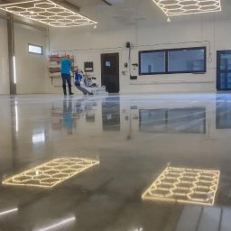 Klimat Professional - Pracownik w studio detailingowym poleruje posadzkę maszyną do polerowania, widoczne odbicia lamp sufitowych na błyszczącej, zabezpieczonej powierzchni.