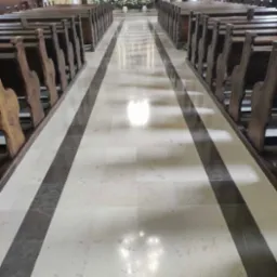 Biało-szara, wypolerowana posadzka z kamiennych płyt w kościele, z rzędami drewnianych ławek po bokach, prowadząca do ołtarza w tle.