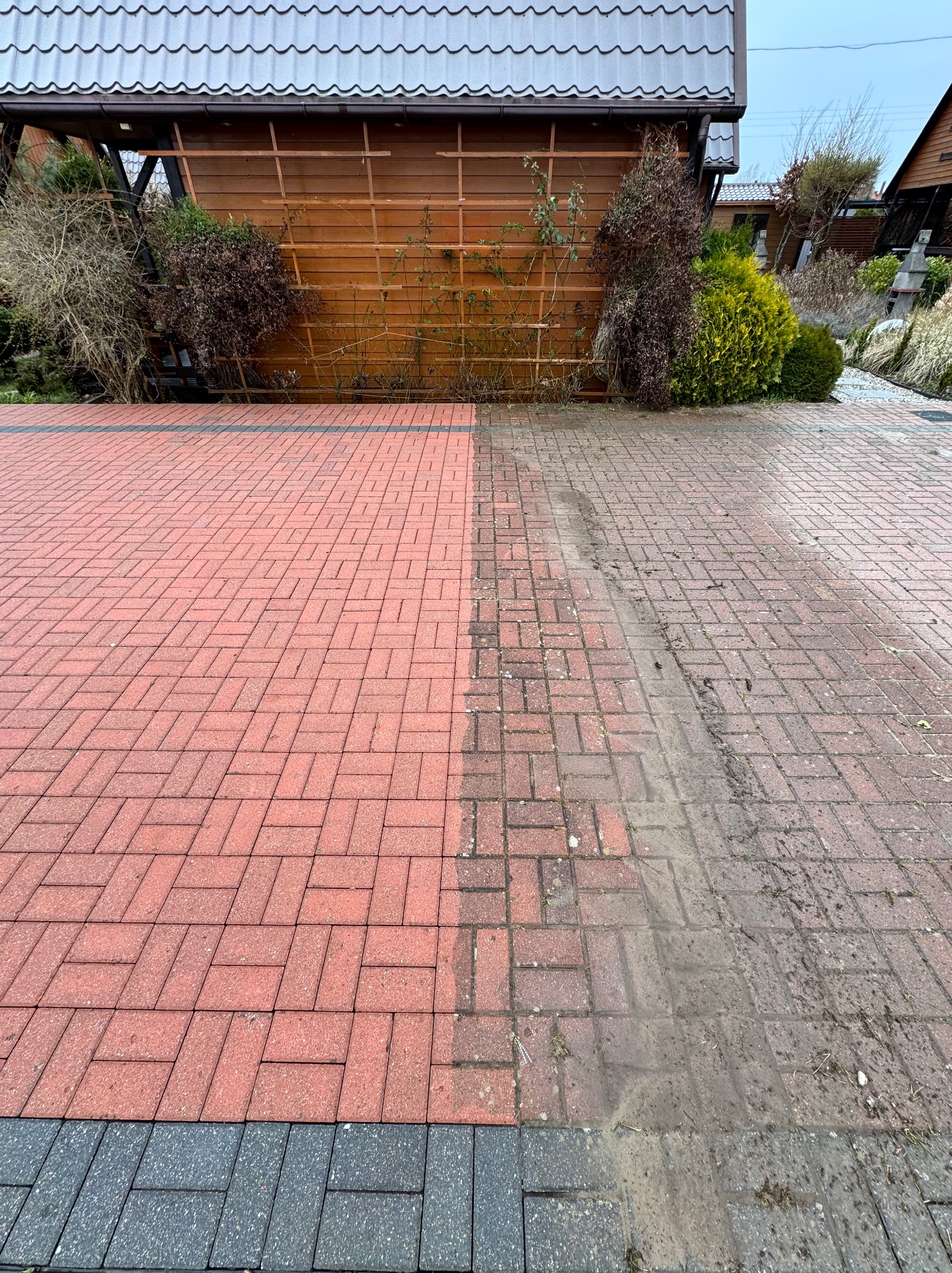 Częściowo wyczyszczona, czerwona kostka brukowa przed drewnianą altaną. Widoczna wyraźna różnica między umytą a brudną powierzchnią.