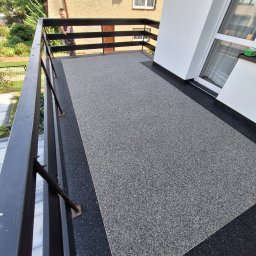 DAMIAN SITEK KAMIENNE DYWANY - Wykończony balkon z szarą, drobnoziarnistą nawierzchnią, czarna listwa przypodłogowa, drewniana balustrada, widok z góry.
