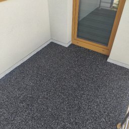 DAMIAN SITEK KAMIENNE DYWANY - Szara, drobnoziarnista powierzchnia balkonu po renowacji, z widocznym oknem balkonowym w drewnianej ramie i fragmentem metalowej balustrady.