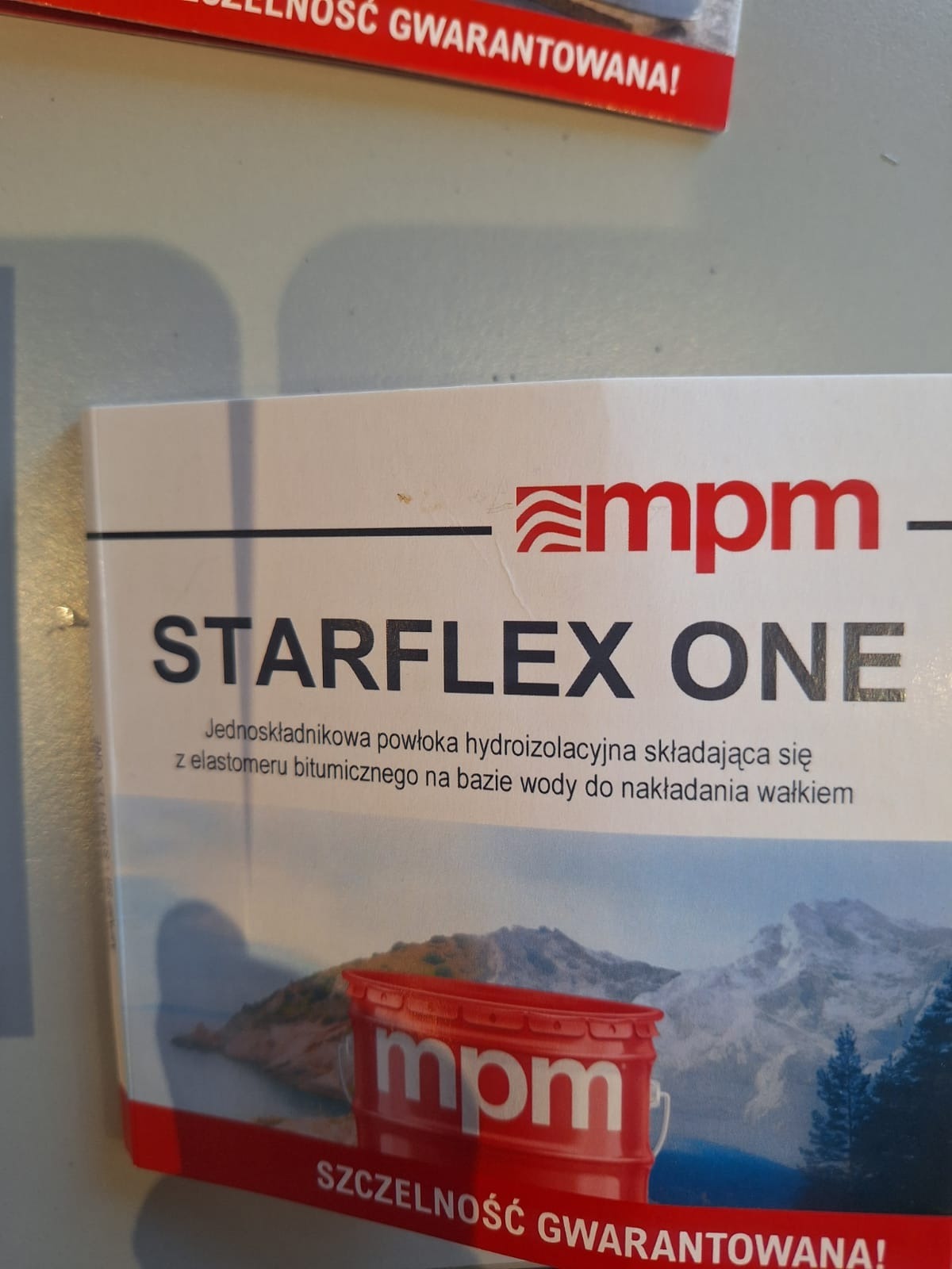 Reklama produktu STARFLEX ONE: jednoskładnikowej powłoki hydroizolacyjnej na bazie elastomeru bitumicznego do nakładania wałkiem, z logo mpm i hasłem 'Szczelność gwarantowana!'.