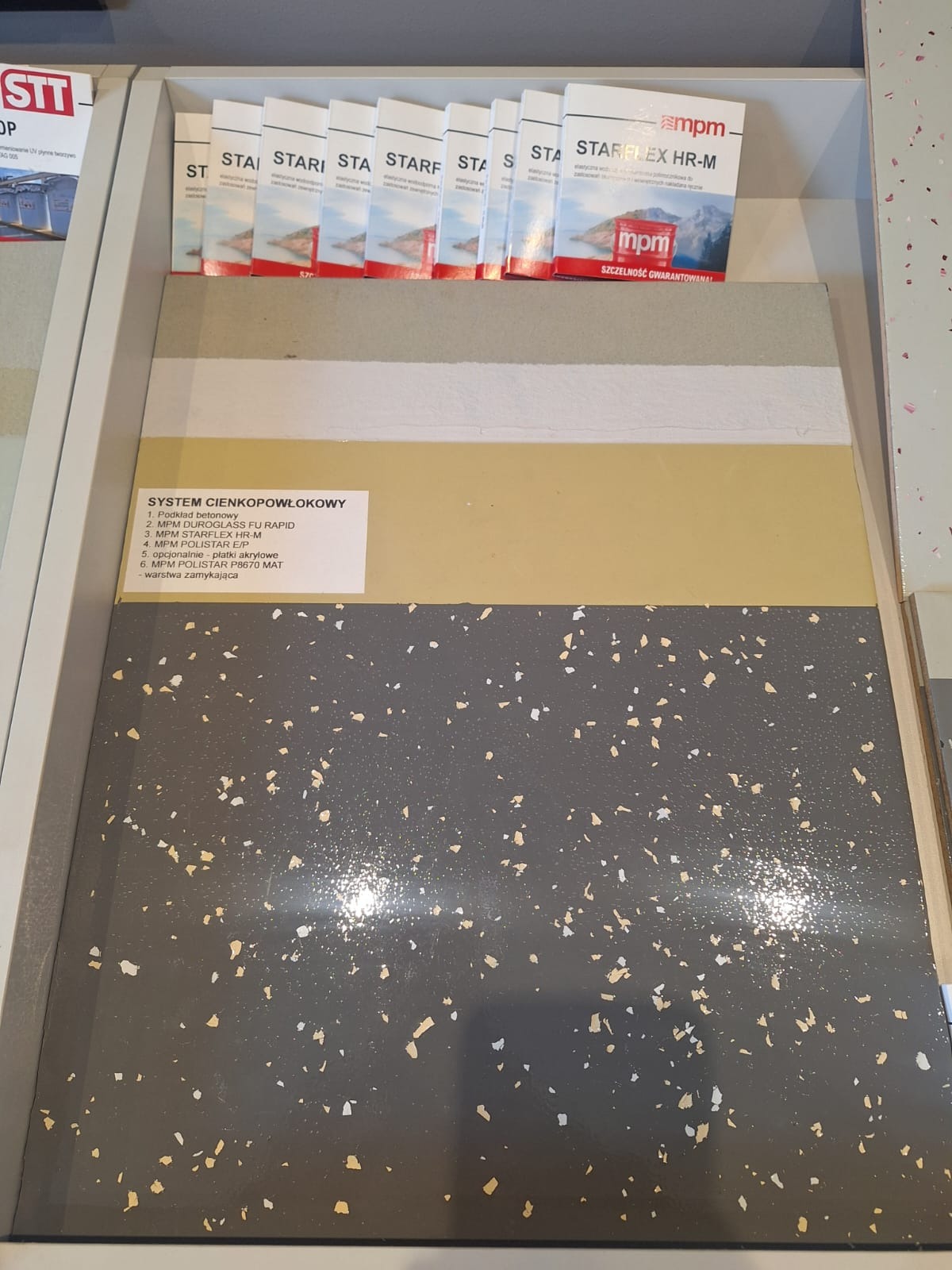Przekrój warstwowy systemu cienkopowłokowego posadzki z widocznymi próbkami różnych kolorów i faktur, prezentowany obok katalogów produktów MPM Starflex HR-M.