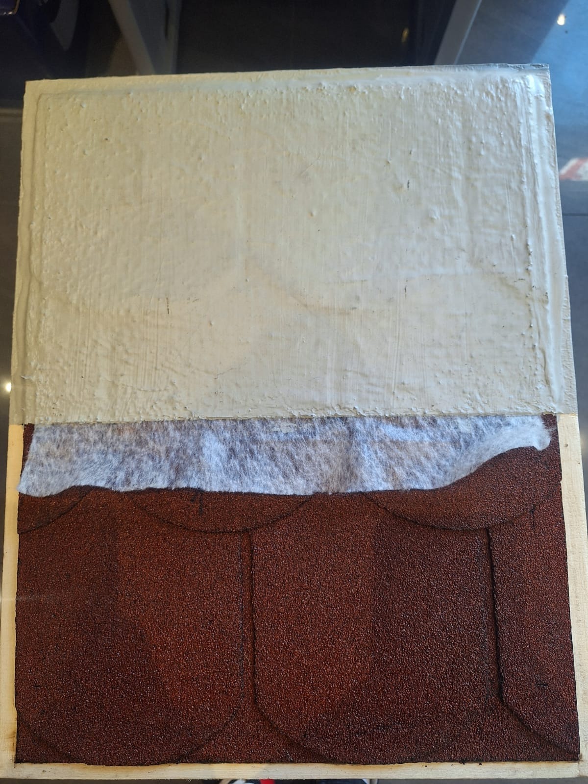 Przekrój warstwowy dachu: brązowe gonty bitumiczne, biała membrana hydroizolacyjna i szara warstwa izolacyjna, prezentacja materiałów.