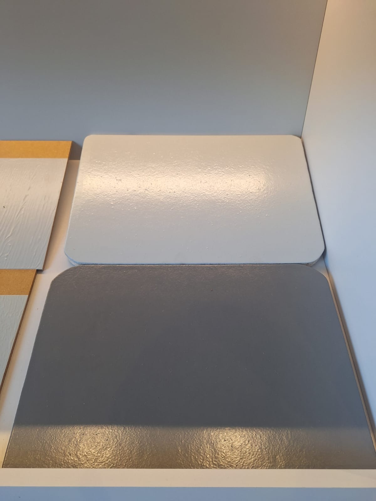 Próbki kolorów i faktur posadzek: szara, biała i drewnopodobna na jasnym tle.