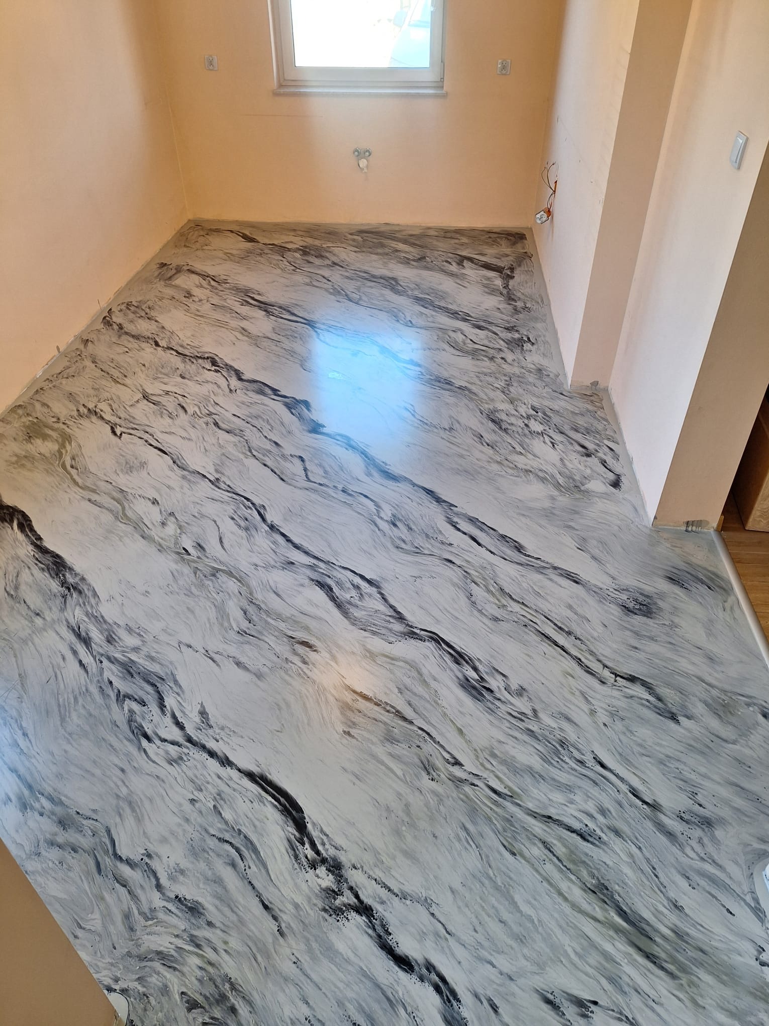 Jasna posadzka w salonie, imitująca marmur, z delikatnym połyskiem. Widoczne ściany w odcieniach beżu i okno z białymi ramami. Nowoczesny design podłogi.