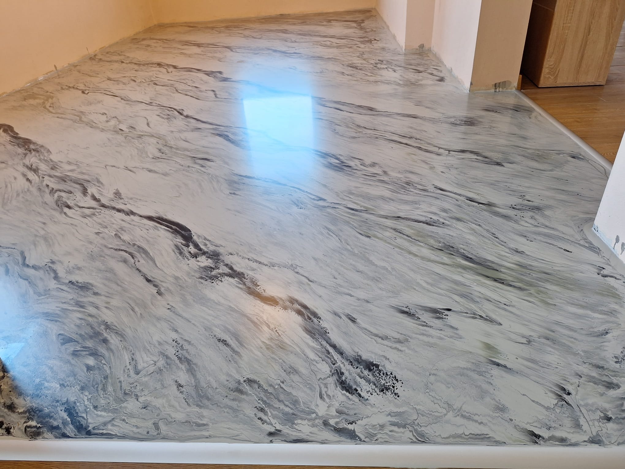 Błyszcząca, marmurkowa posadzka żywiczna w odcieniach szarości i bieli, wykonana w Julianowie. Widoczny refleks światła i gładka powierzchnia.