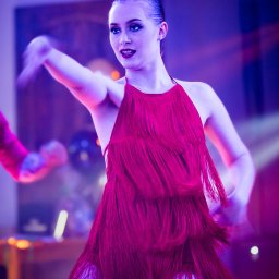 Zbigniew Zięba - Kobieta w czerwonej sukience z frędzlami tańczy na scenie oświetlonej fioletowym światłem.