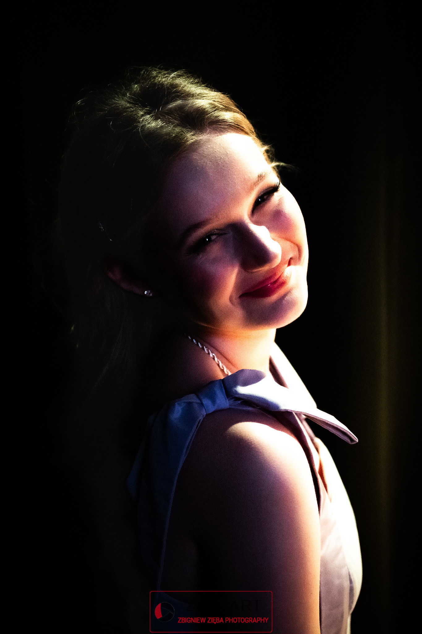 Portret uśmiechniętej blondynki w sukni z odkrytymi ramionami, wykonany w Sianowie w kontraście światła i cienia.