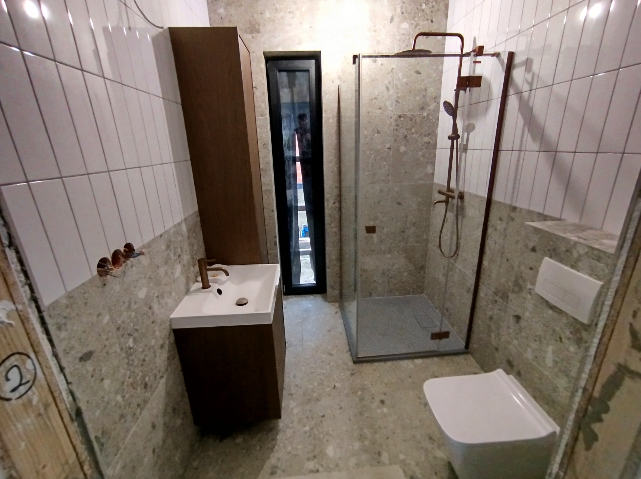 Nowoczesna łazienka z kabiną prysznicową, umywalką z szafką w kolorze drewna i toaletą, wykończona płytkami imitującymi kamień i białymi płytkami na ścianach.