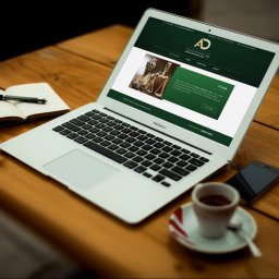 Kancelaria Adwokacka Adwokat Aleksandra Dzida - Laptop z otwartą stroną internetową kancelarii adwokackiej na drewnianym stole, obok notatnik z długopisem, smartfon i filiżanka kawy.