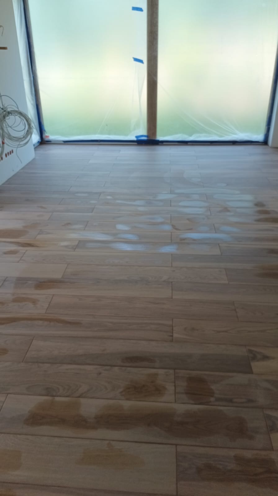 Nowo ułożona podłoga z płytek imitujących drewno, widoczne ślady po czyszczeniu, okno zabezpieczone folią malarską.