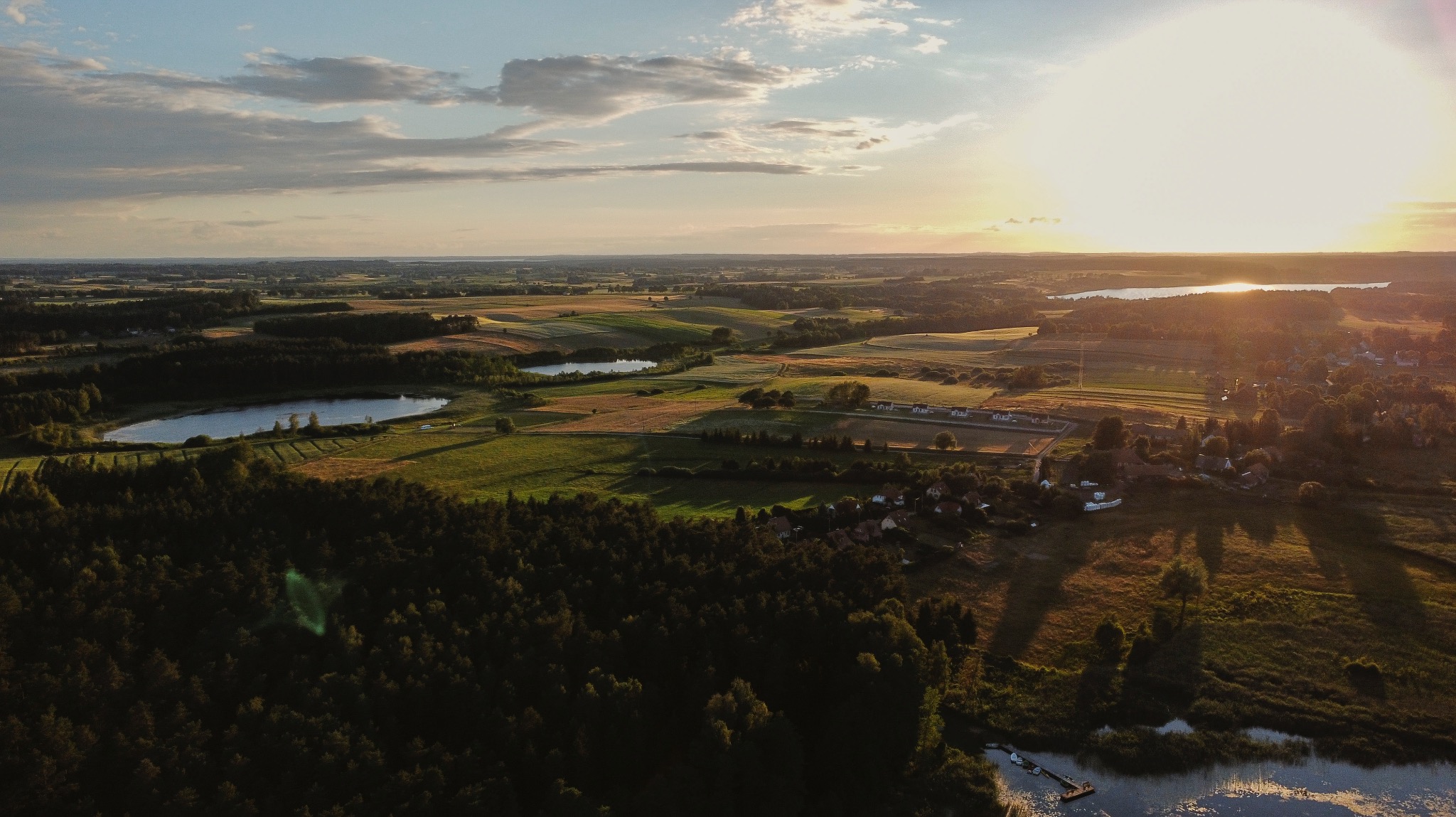 Panoramiczny widok z lotu ptaka na krajobraz wiejski o zachodzie słońca, z jeziorami, polami i lasami.