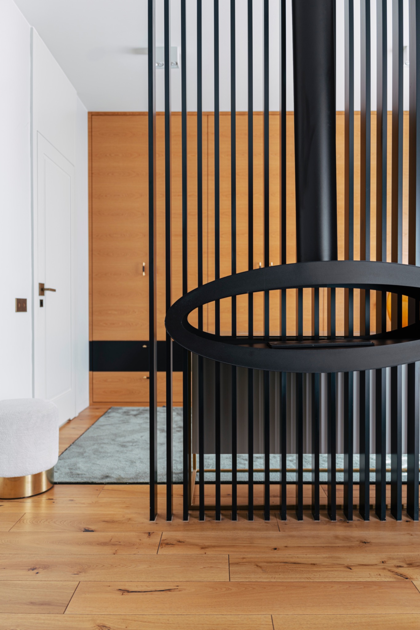 Nowoczesny salon z drewnianą podłogą, ażurową ścianką działową i designerskim, wiszącym kominkiem w kolorze czarnym.