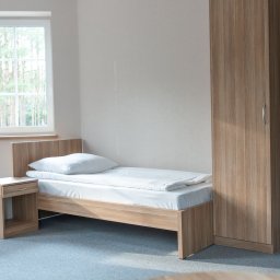 PRYWATNY OŚRODEK LECZENIA UZALEŻNIEŃ EXIT - Pokój z pojedynczym łóżkiem, szafką nocną i szafą w odcieniach drewna, widok na las przez okno.