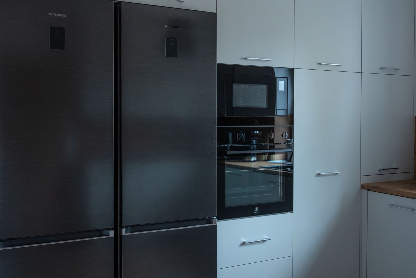 Nowoczesna kuchnia z ciemnoszarą lodówką Samsung side-by-side i zabudowanymi urządzeniami Electrolux w jasnych szafkach.