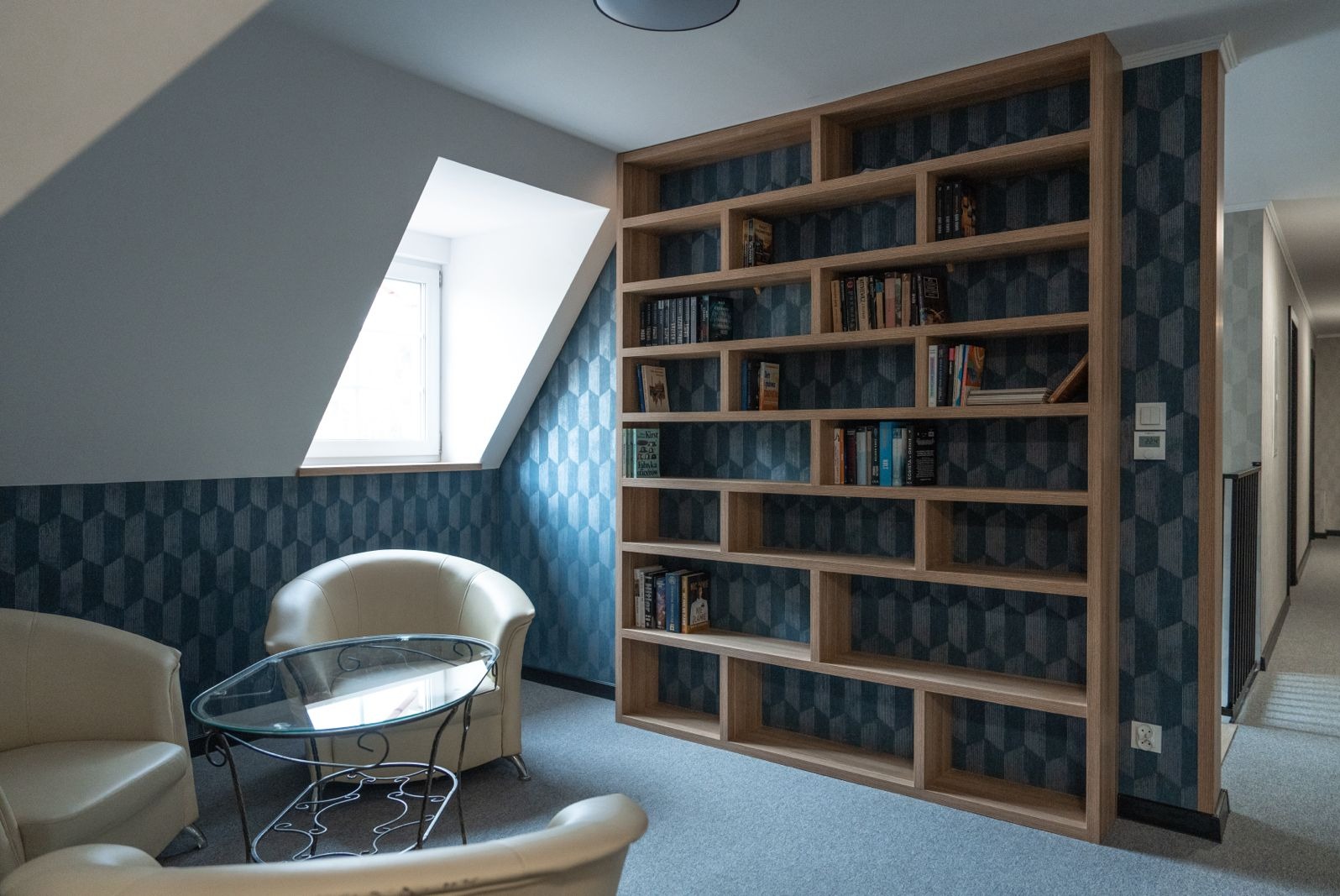 Kącik relaksacyjny w Starym Licheniu: Dwa kremowe fotele klubowe i szklany stolik kawowy na tle ściany z geometryczną tapetą i drewnianego regału z książkami.