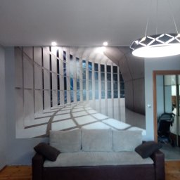 firma remontowo-budowlana Cycuś-Glancuś.pl - Wnętrze pokoju z fototapetą imitującą widok z okna na morze i niebo, szary narożnik z poduszkami, nowoczesna lampa sufitowa