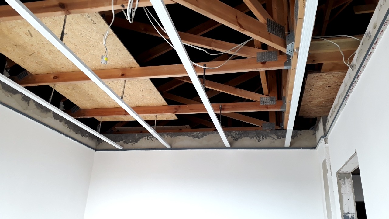 Montaż profili sufitowych podwieszanych na drewnianej konstrukcji stropu, widoczne przewody elektryczne i płyta OSB.