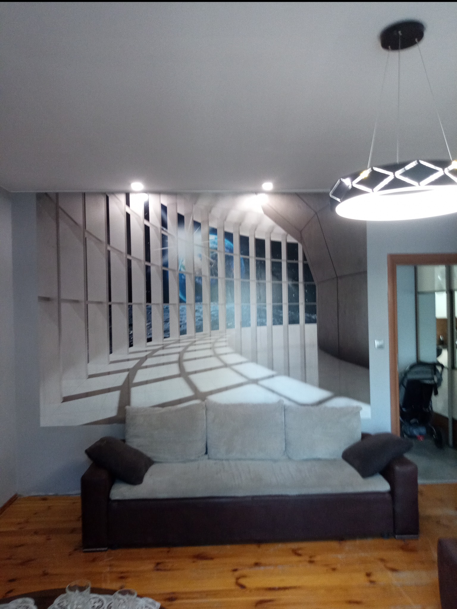 Wnętrze pokoju z fototapetą imitującą widok z okna na morze i niebo, szary narożnik z poduszkami, nowoczesna lampa sufitowa