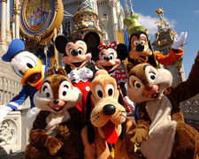 Grupa postaci z bajek Disneya (Mickey Mouse, Minnie Mouse, Donald Duck, Goofy, Pluto, Chip i Dale) pozuje na tle zamku w Eurodisneylandzie, widoczne detale architektoniczne i dekoracje.