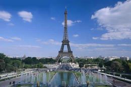 Wieża Eiffla w Paryżu widziana z perspektywy fontanny, błękitne niebo z chmurami w tle.