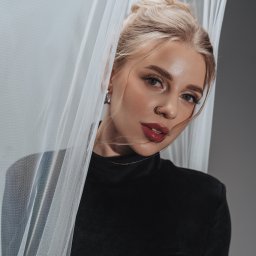 Anastasiia Martynets - Portret blondwłosej kobiety z piercingiem w nosie, pozującej za delikatną, białą tkaniną na szarym tle.