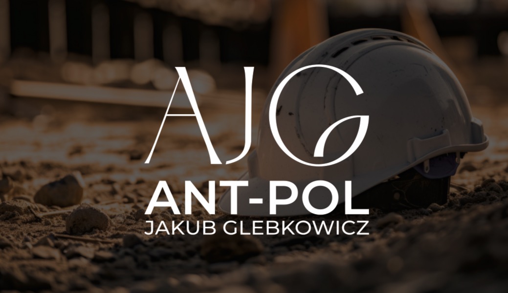 Biały kask budowlany na gruzowisku z logo firmy AJG ANT-POL Jakub Glebkowicz. Stonowana kolorystyka, ciepłe światło. Elementy budowlane w tle.