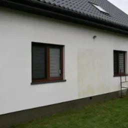 Boczna ściana domu z widocznymi zabrudzeniami i fragmentem rusztowania, sugerująca etap przygotowania do prac elewacyjnych.