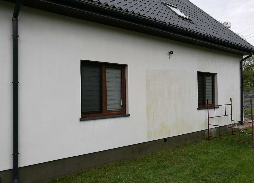 Boczna ściana domu z widocznymi zabrudzeniami i fragmentem rusztowania, sugerująca etap przygotowania do prac elewacyjnych.