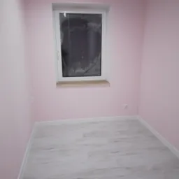 Pomalowane na różowo wnętrze pokoju z białymi listwami przypodłogowymi i szarą podłogą, okno zabezpieczone folią.